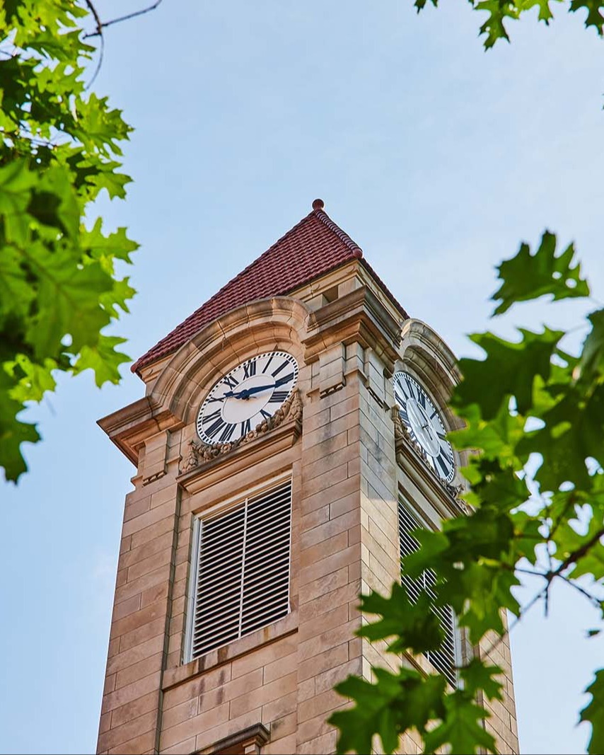 stock-photo-detail-of-limestone-clock-tower-surrounded-by-green-leaves-2243770263